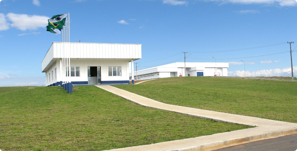 Foto horizontal, com vista frontal da sede administrativa de Guarapuava, com dois prédios brancos de alvenaria, extenso gramado à frente e céu azul claro.